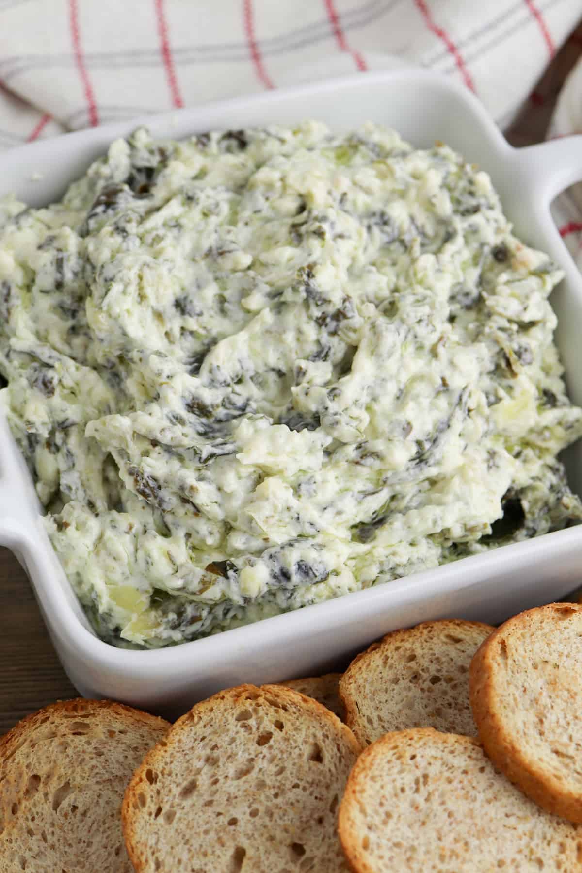 creamy crockpot spinach and artichoke dip in white bowl served with small pieces of bread for dipping