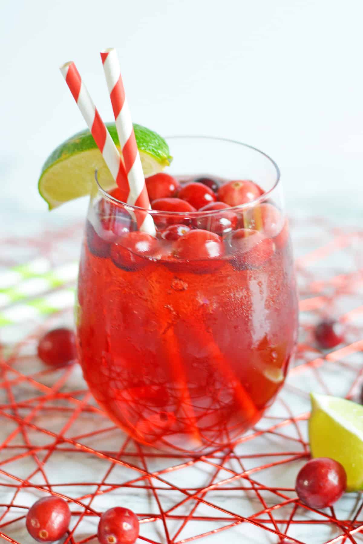 Vodka cranberry cocktail in short wine glass garnished with lime wedge and fresh cranberries