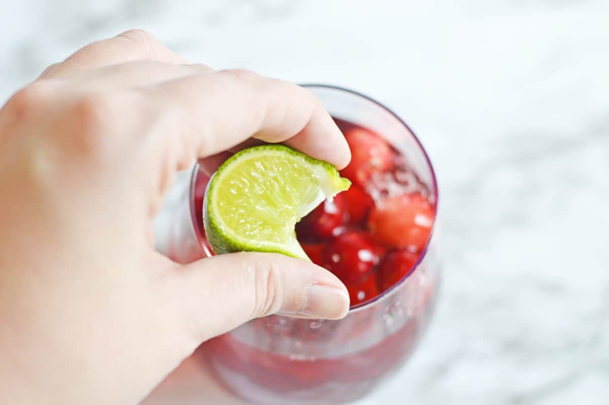 hand squeezing lime wedge into vodka cranberry cocktail