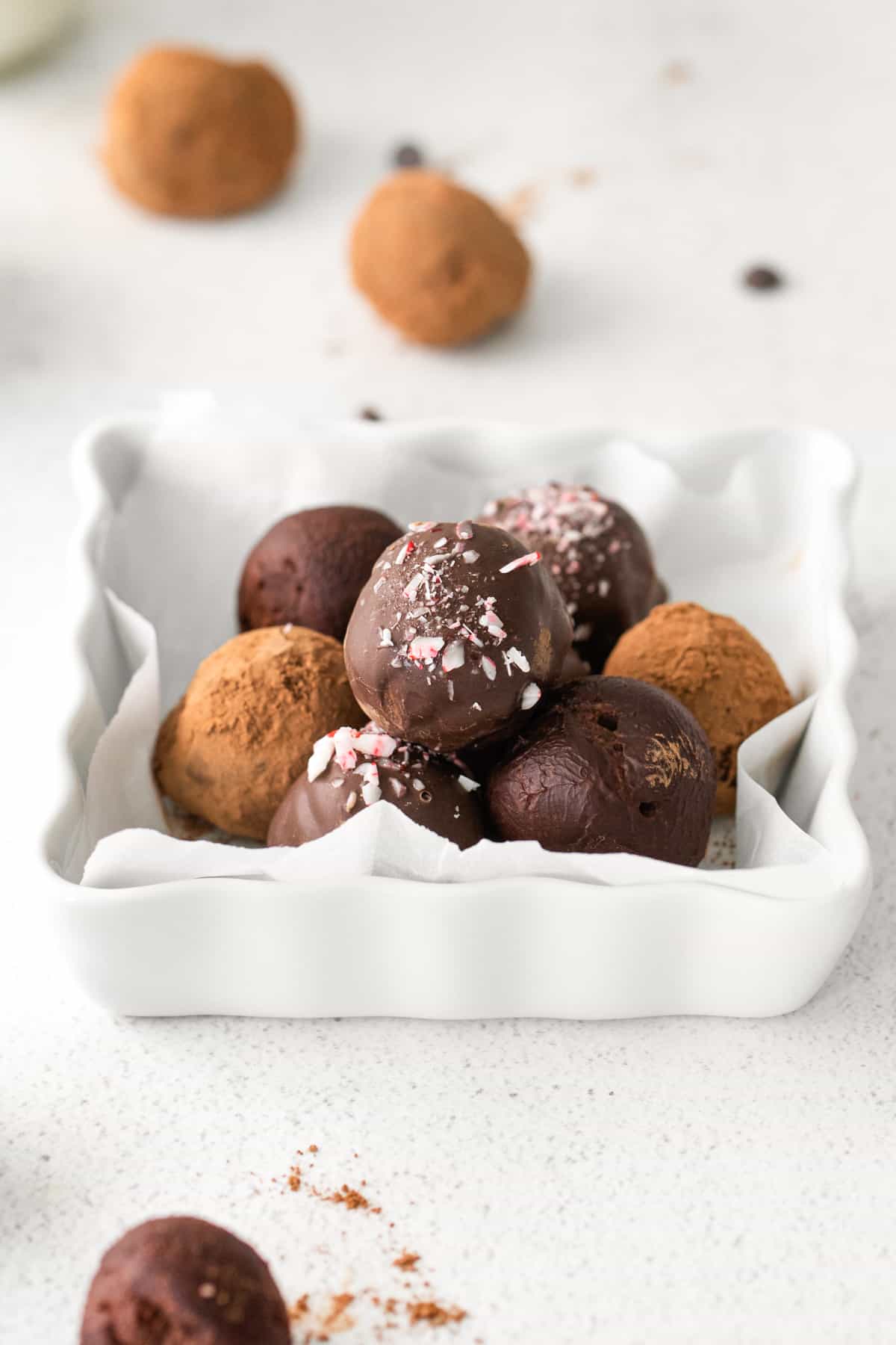 dark chocolate truffles in serving plate, some rolled in cocoa powder, some plain, and some coated in chocolate topped with crushed peppermint candy