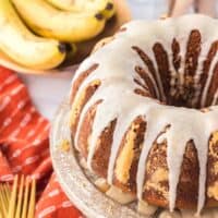 Banana bundt cake with powdered sugar glaze poured over the top and with bananas and a fork in the background.