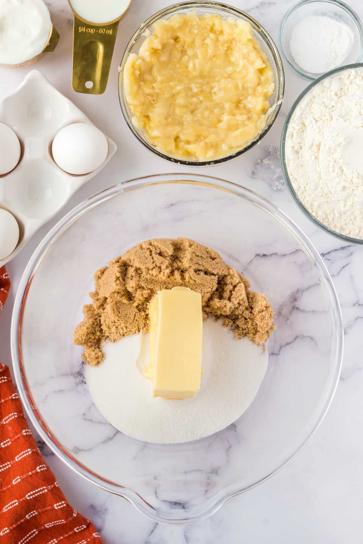 large glass mixing bowl with brown sugar, granulated sugar, and butter.