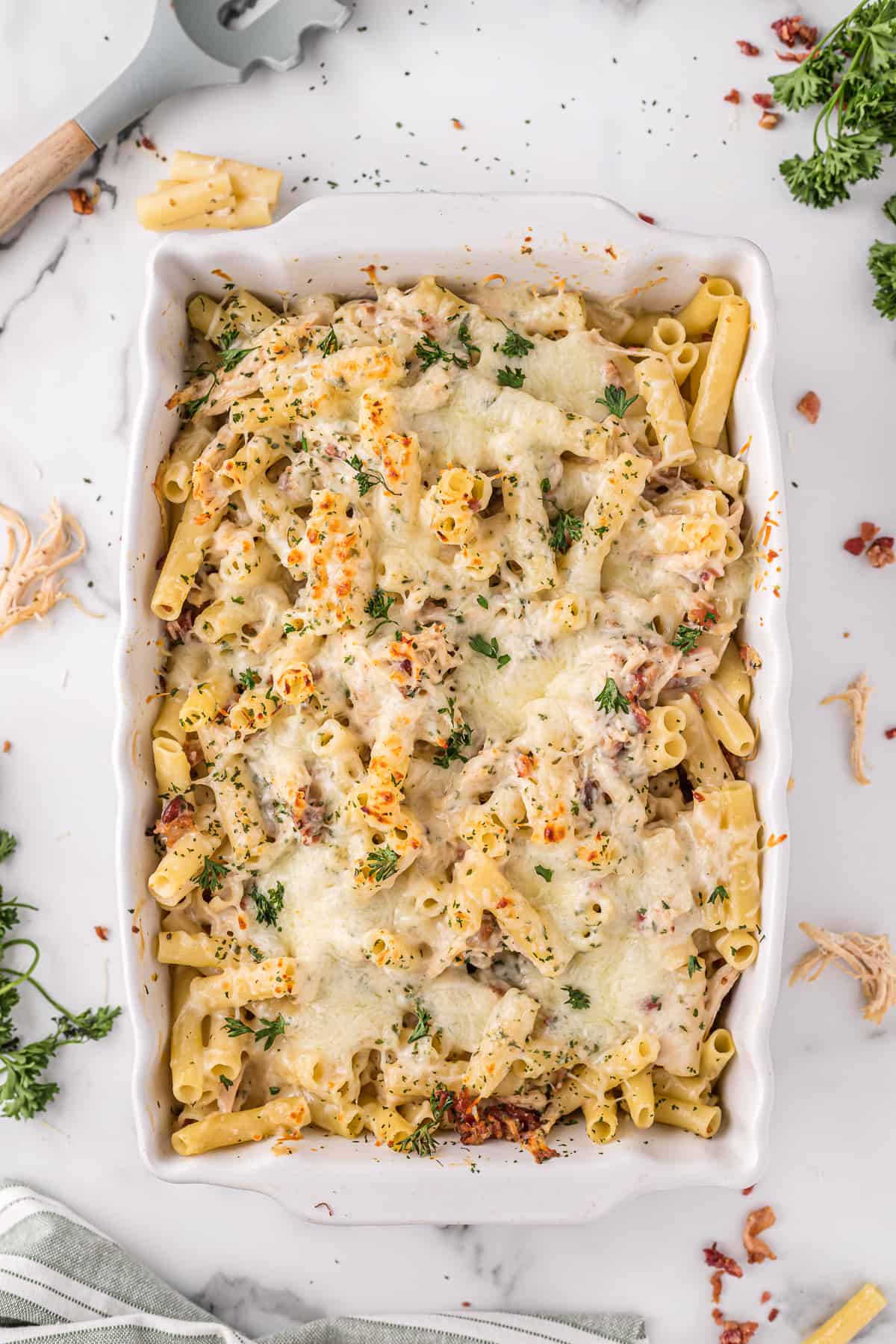 Chicken alfredo pasta bake with bacon and parsley on top, in a 9 x 13 casserole dish