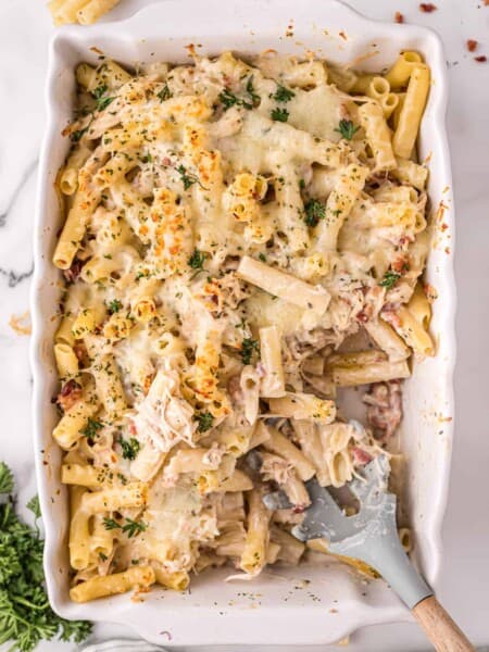 Chicken Bacon Alfredo Pasta Bake in a 9 x 13 casserole dish with a missing portion and serving spoon set inside