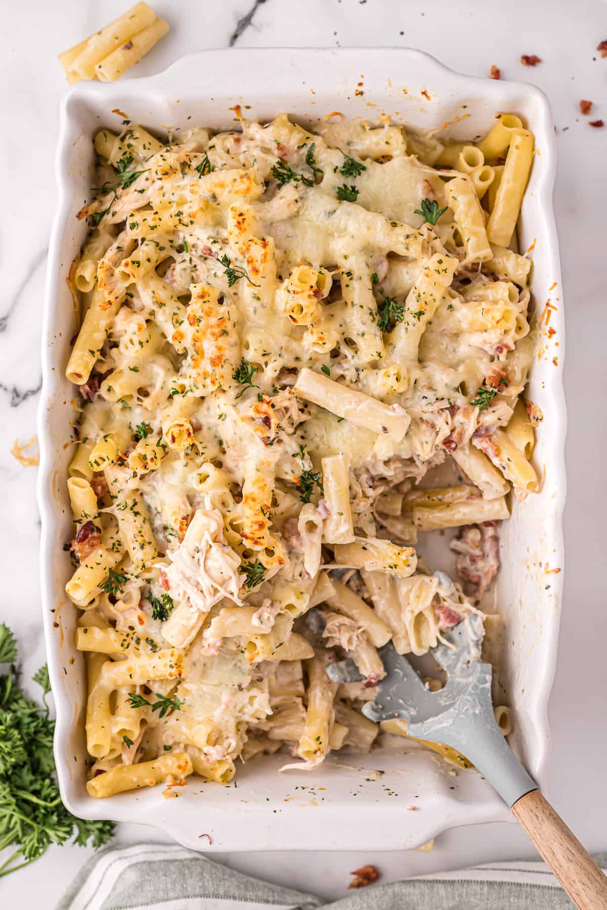 Chicken Bacon Alfredo Pasta Bake in a 9 x 13 casserole dish with a missing portion and serving spoon set inside