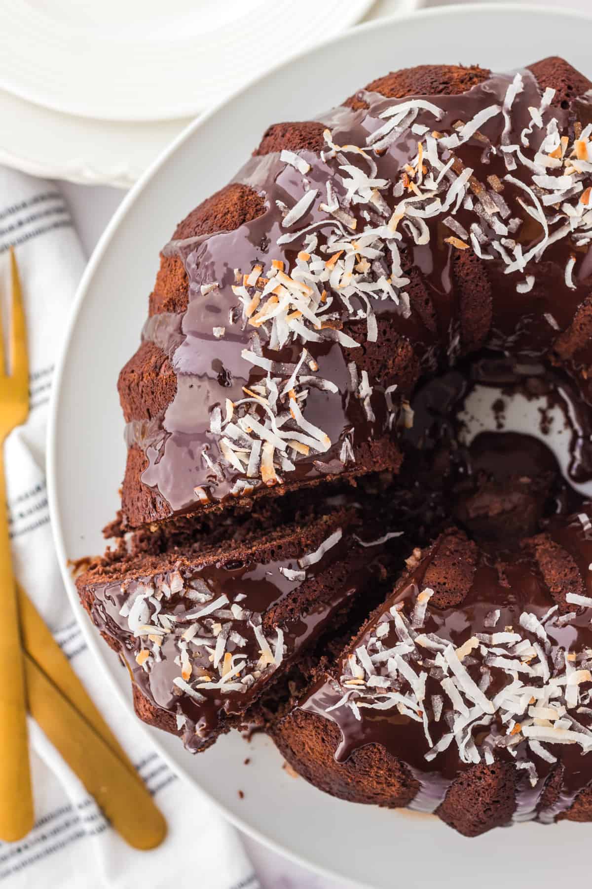 Chocolate coconut bundt cake with chocolate ganache and toasted coconut with a single slice cut out.