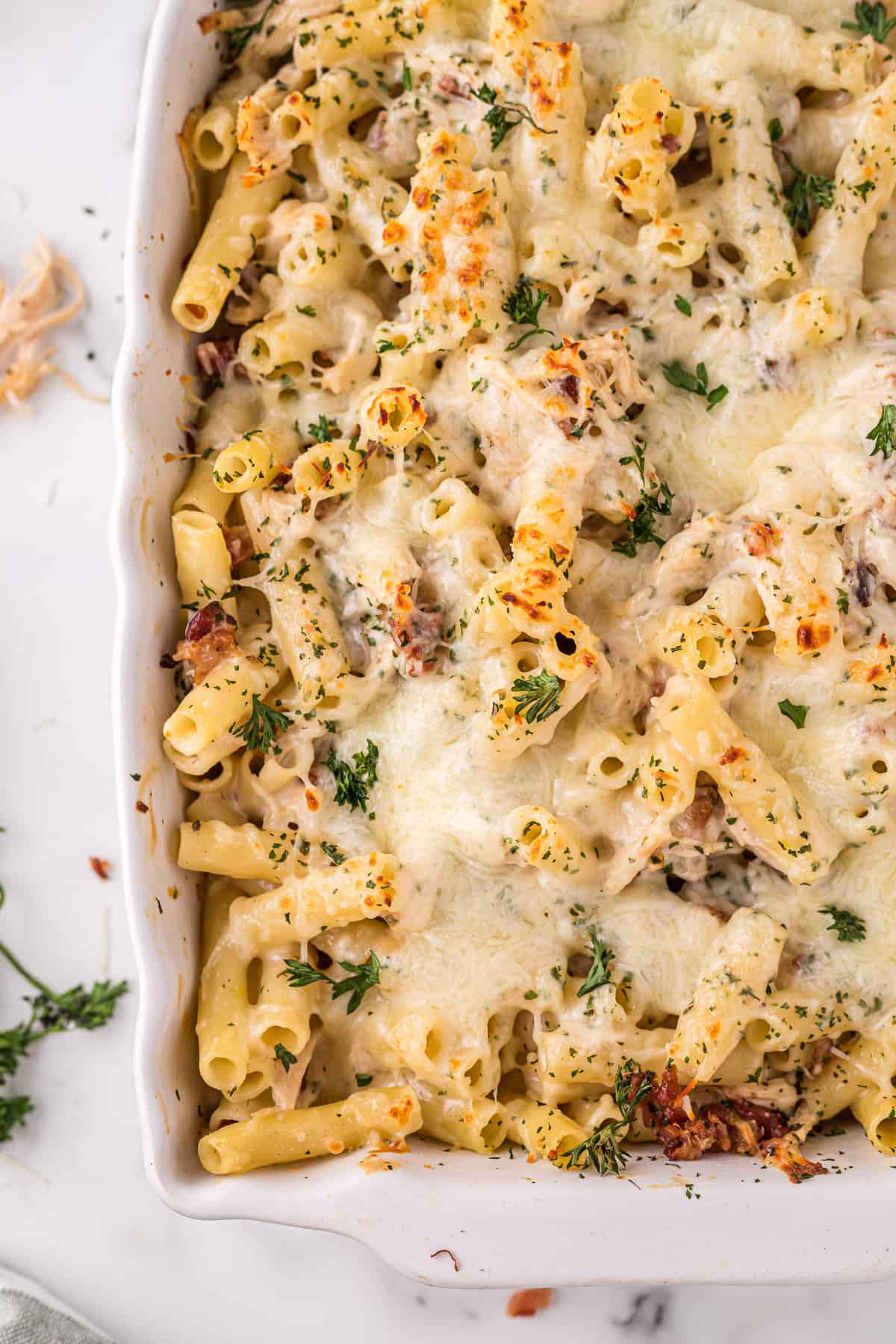 Corner of baking dish with a cheesy chicken bacon alfredo pasta bake garnished with parsley