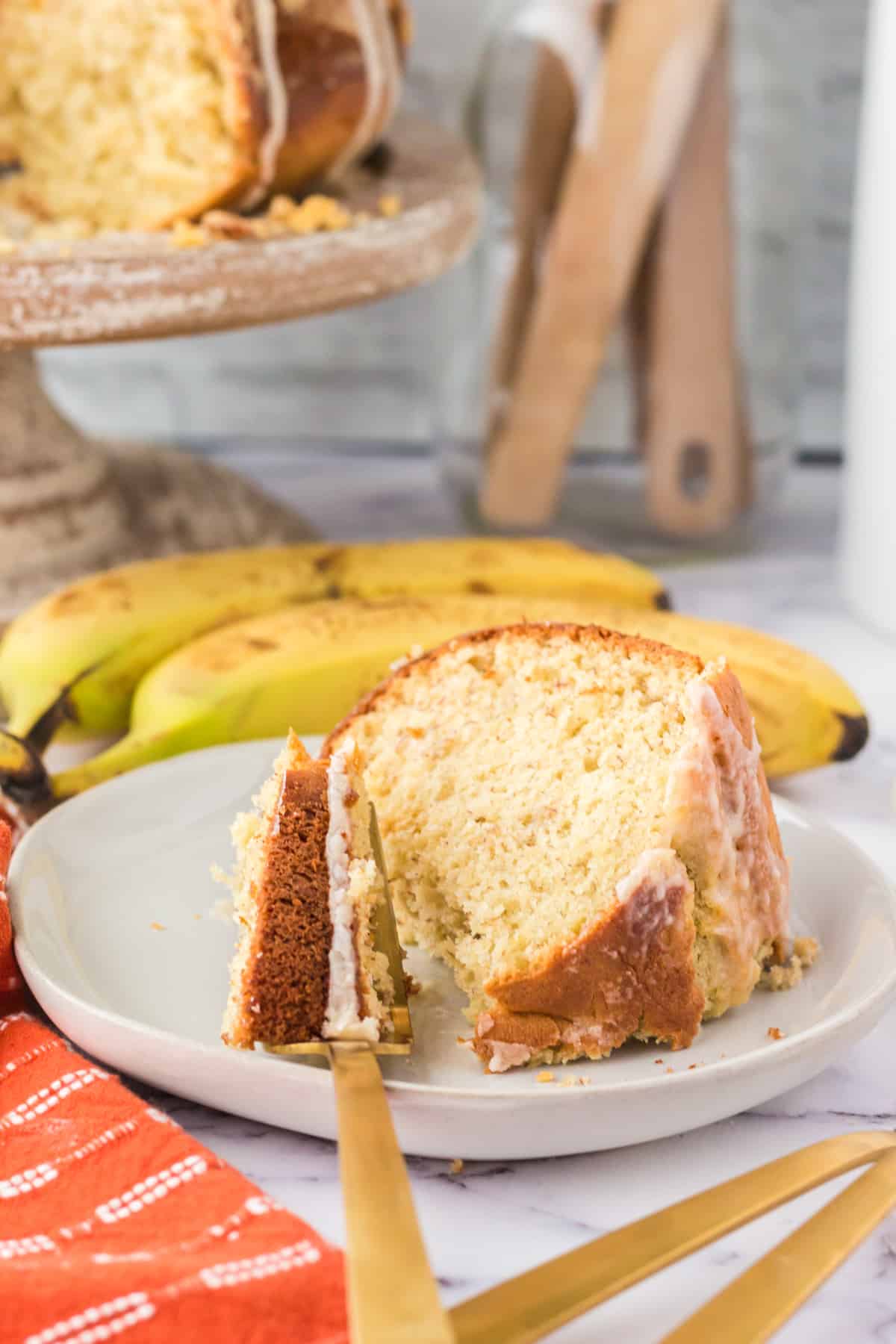 Slice of moist banana cake on white plate with a piece taken out of it and on a fork.