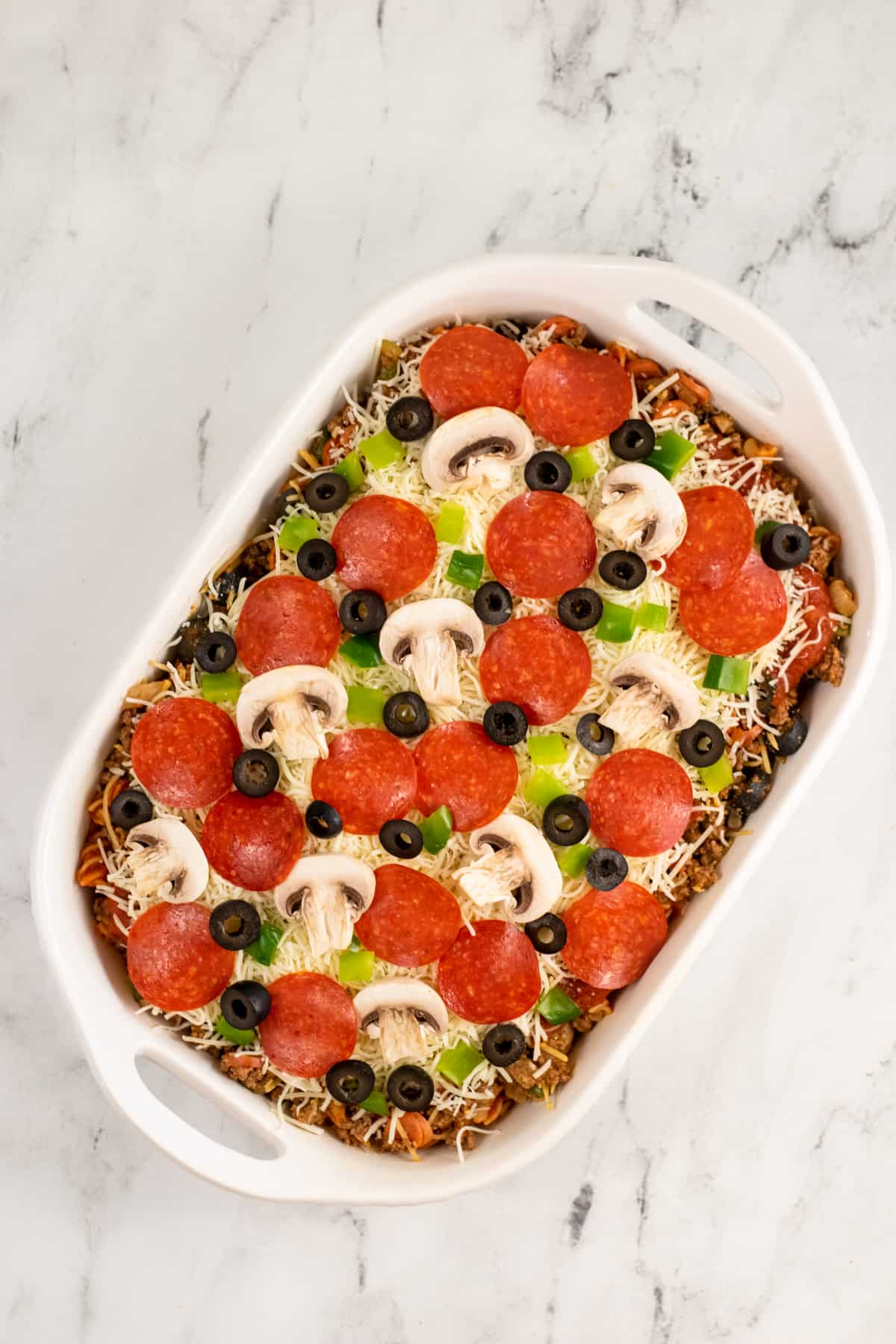 Casserole topped with large pepperoni, sliced mushrooms, chopped green peppers, and sliced black olives