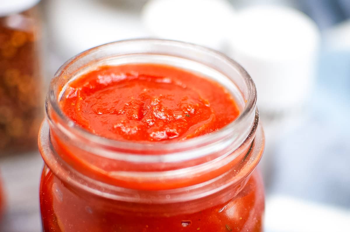 Close up photo of thick pizza sauce in a glass jar.