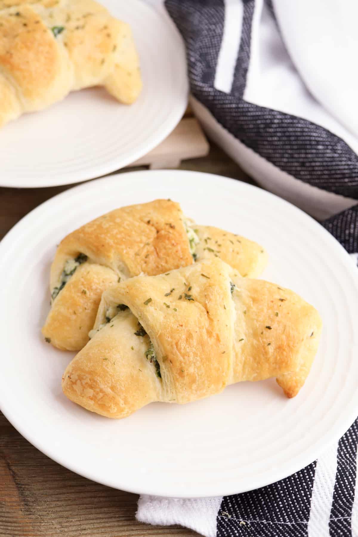 Spinach artichoke crescent rolls on whit plate with another plate of rolls in the background
