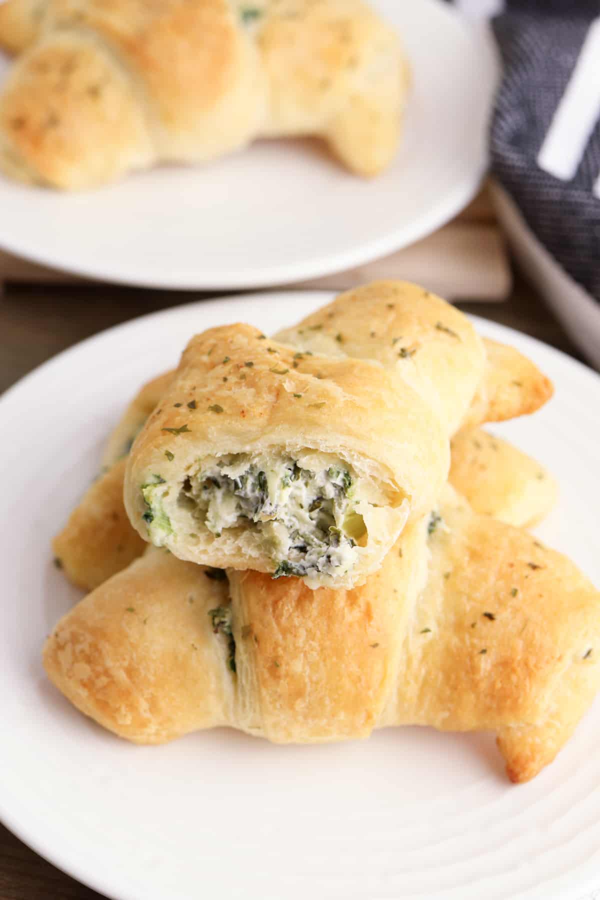 Three spinach artichoke crescent rolls on a plate, one with a bite taken out of it to show the creamy and cheesy spinach dip inside of it.