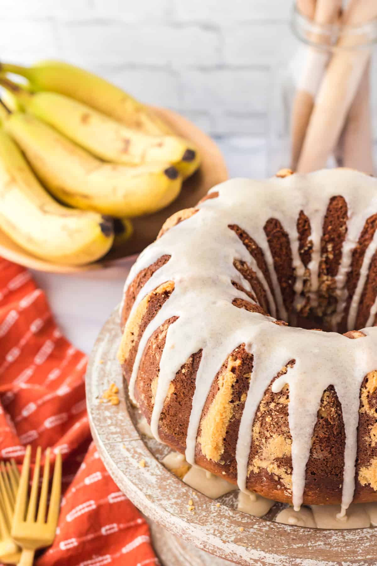 Banana bundt cake with powdered sugar glaze poured over the top and with bananas and a fork in the background.