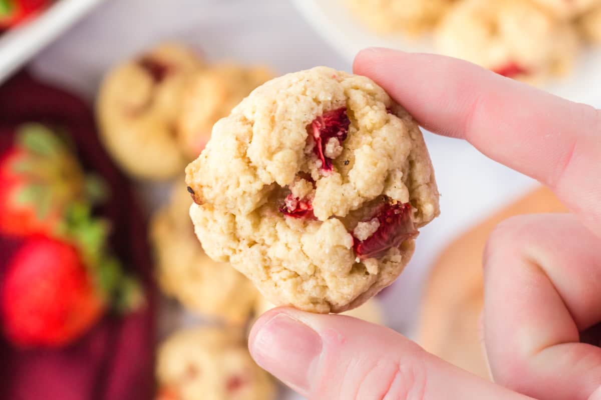 Person holding bite-sized strawberry cookie in between two fingers