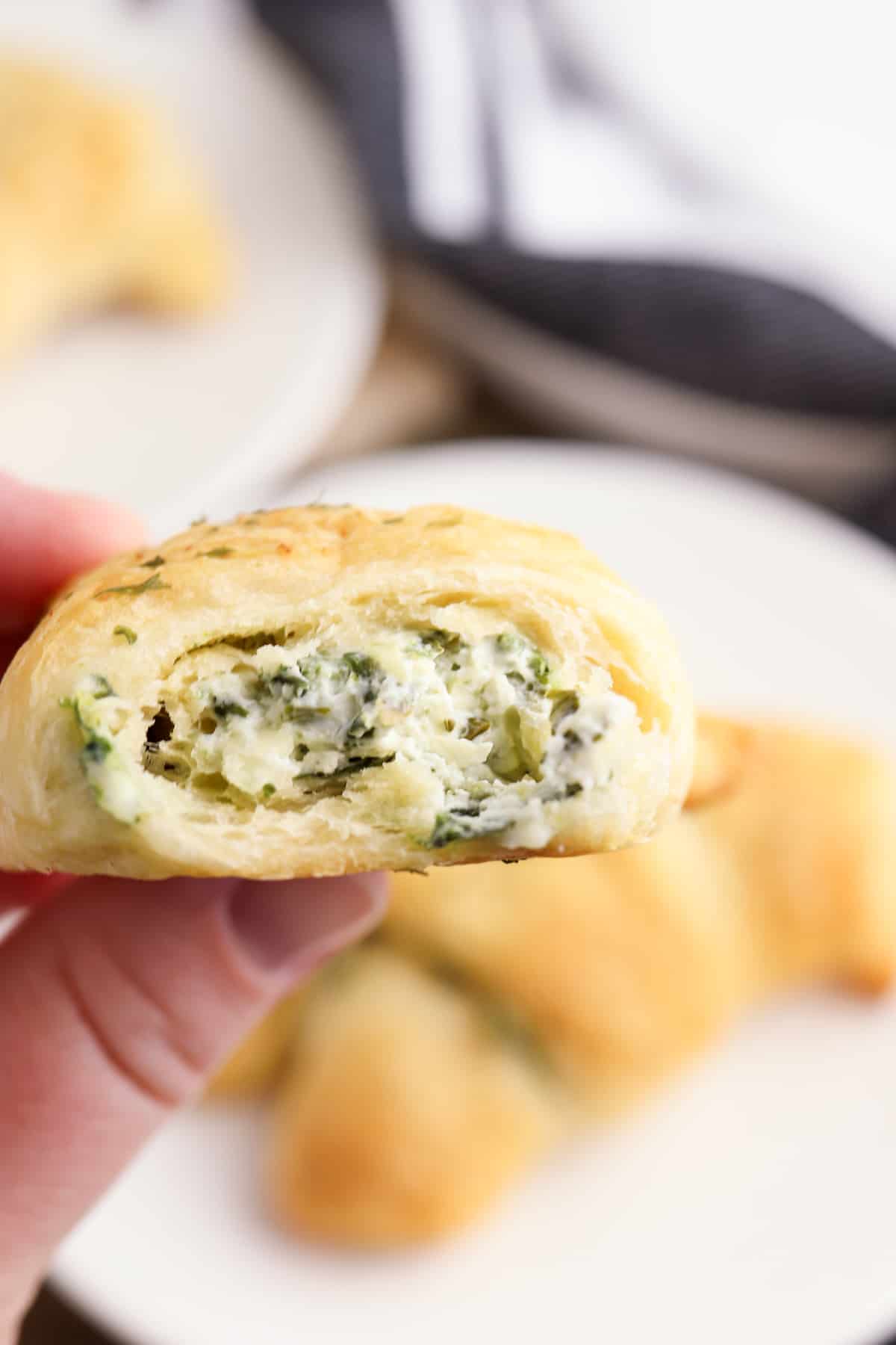 hand holding a spinach dip stuffed crescent roll with a bite taken out of it