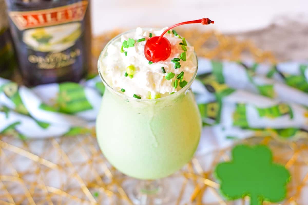 Boozy shamrock shake with whipped cream, green sprinkles, and a cherry. 
