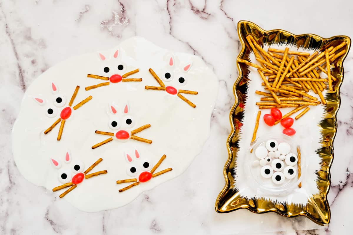 Plate with pretzel sticks, pink jelly beans, and candy eyes next to melted white candy with bunny faces created with the candy.