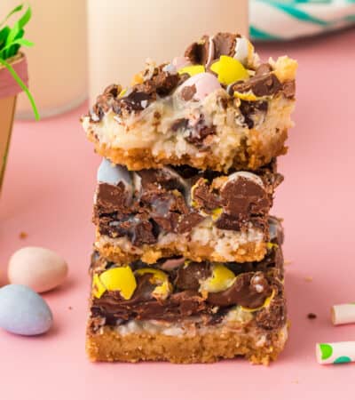 Easter dessert bars with sweetened condensed milk, chocolate chips, coconut, and chocolate eggs stacked on top of one another with top bar missing a bite.