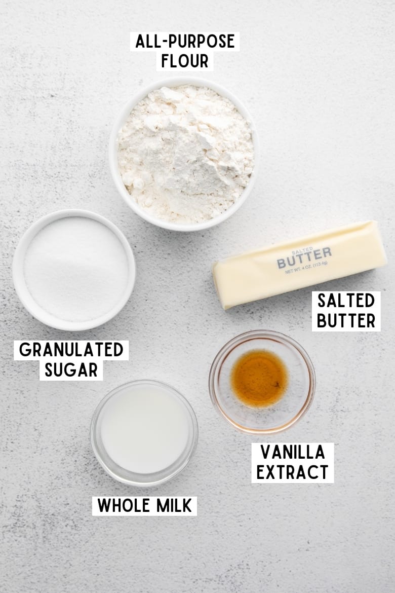 Stick of salted butter and the following ingredients in bowls: purpose flour, granulated sugar. vanilla extract, whole milk.