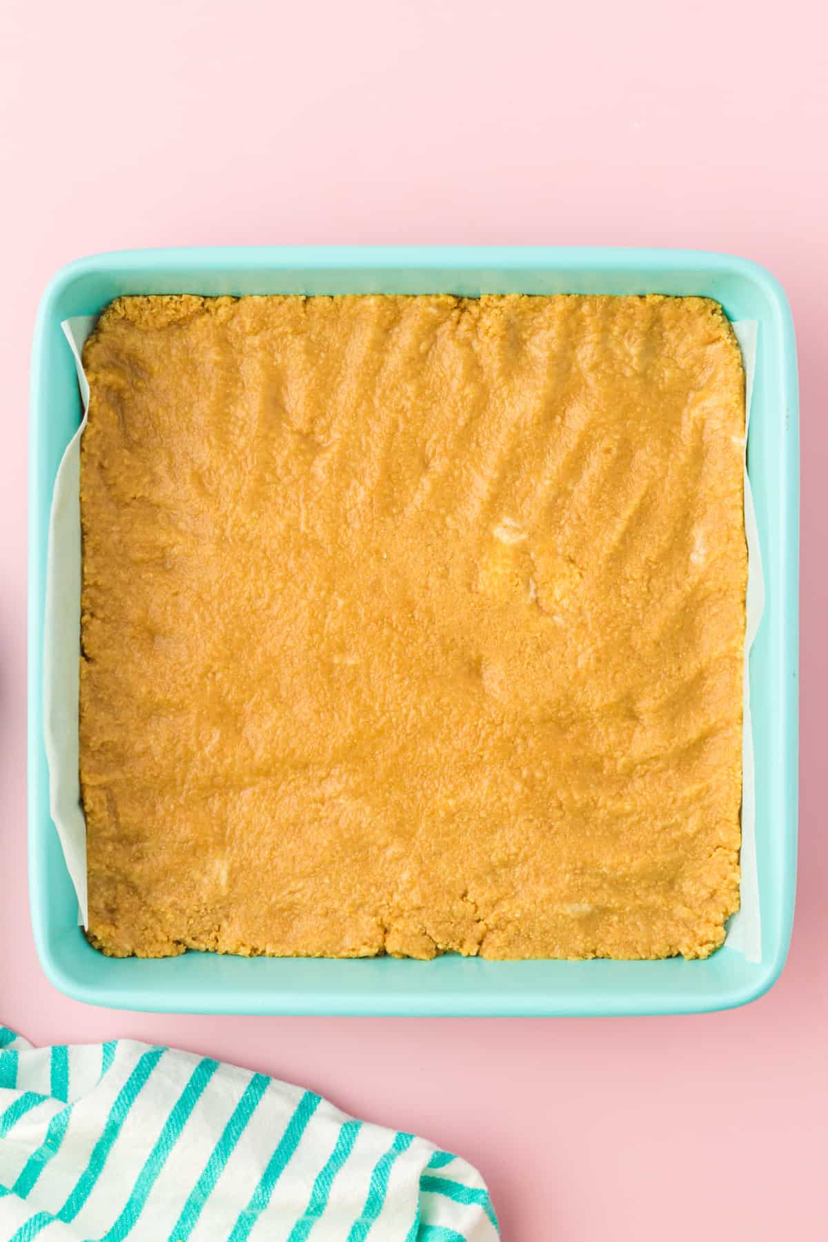 Golden oreo cookie crust pressed into light blue square baking pan.
