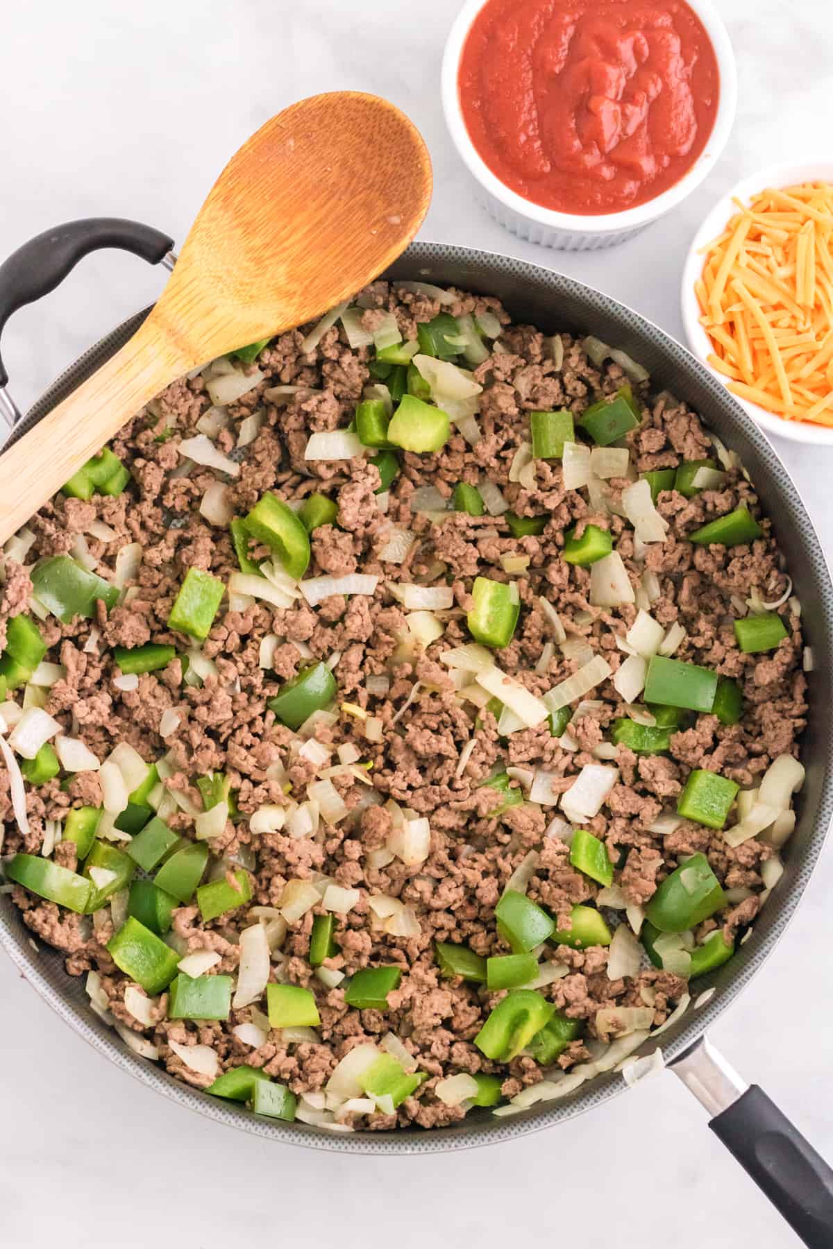 Browned ground beef in a large skillet with chopped peppers and onions.