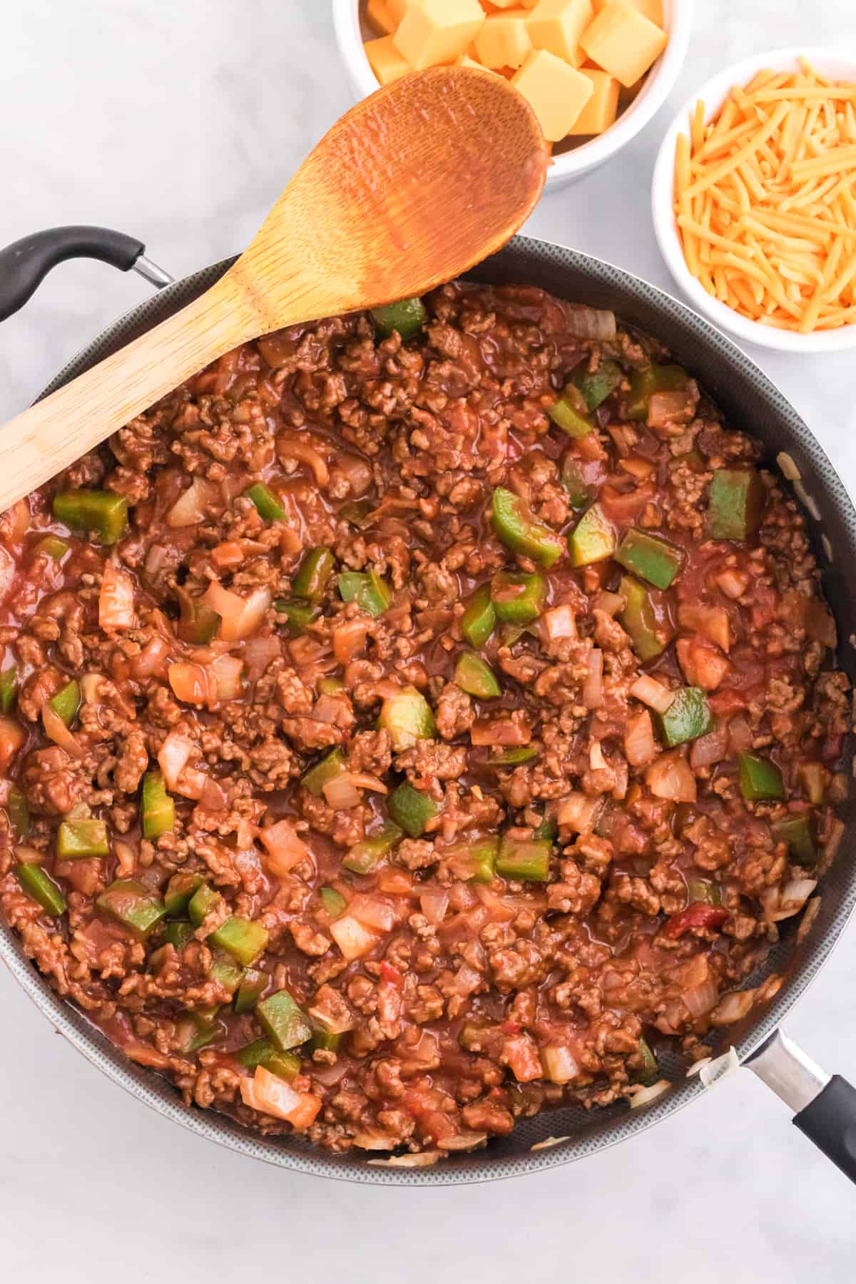 Cooked ground beef, peppers, and and onions covered in manwich sloppy joe sauce in a large skillet.