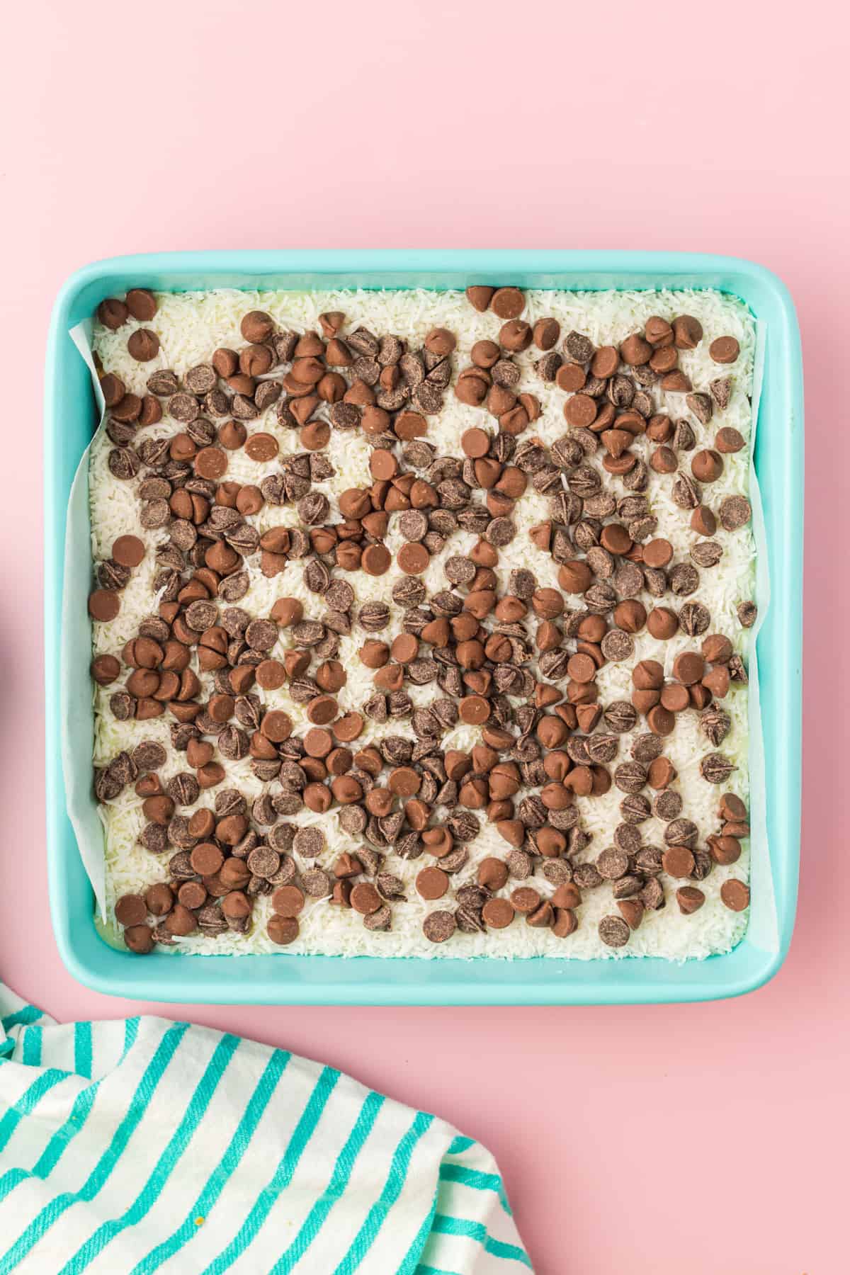 Square casserole dish with shredded coconut topped with chocolate chips.