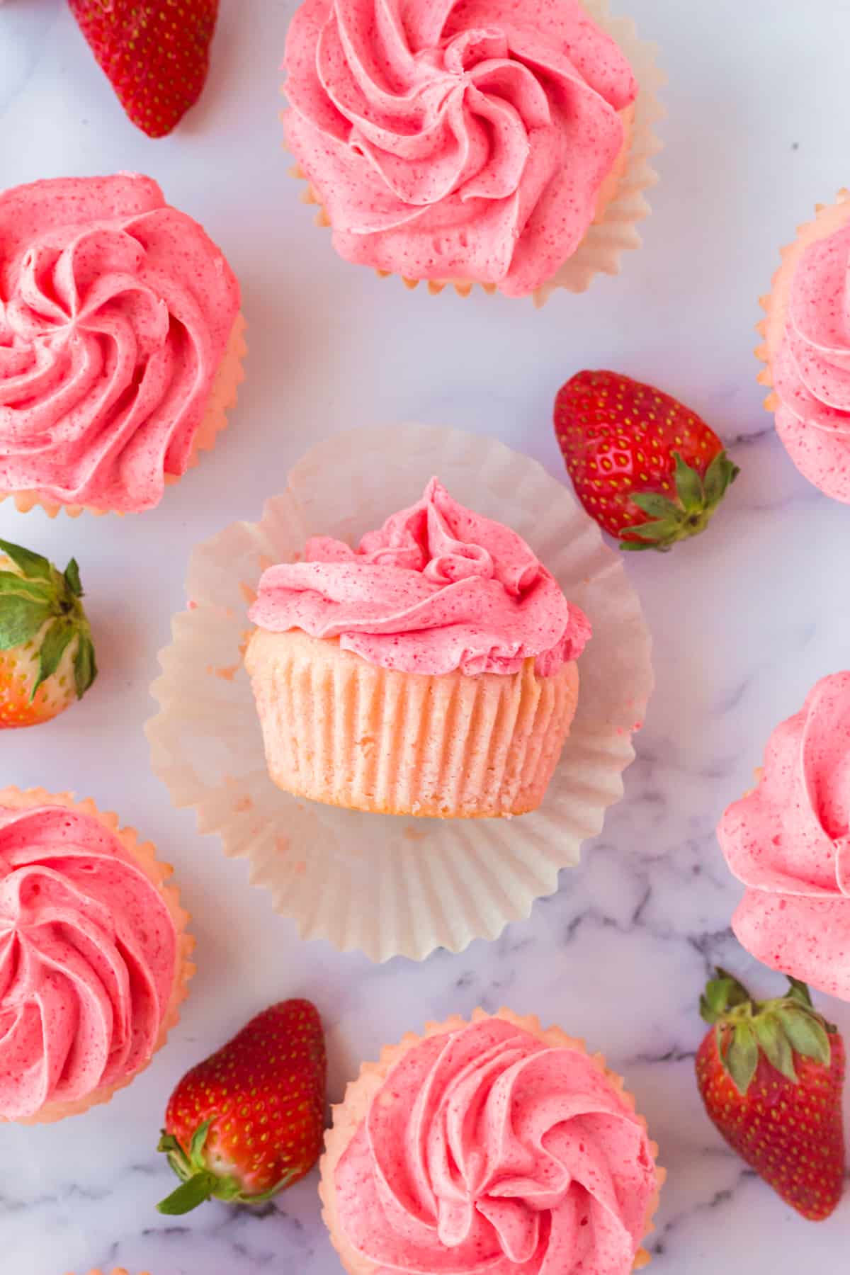 Strawberry Filled Cupcakes with Strawberry Jello Buttercream on marble countertop with fresh strawberries around them.