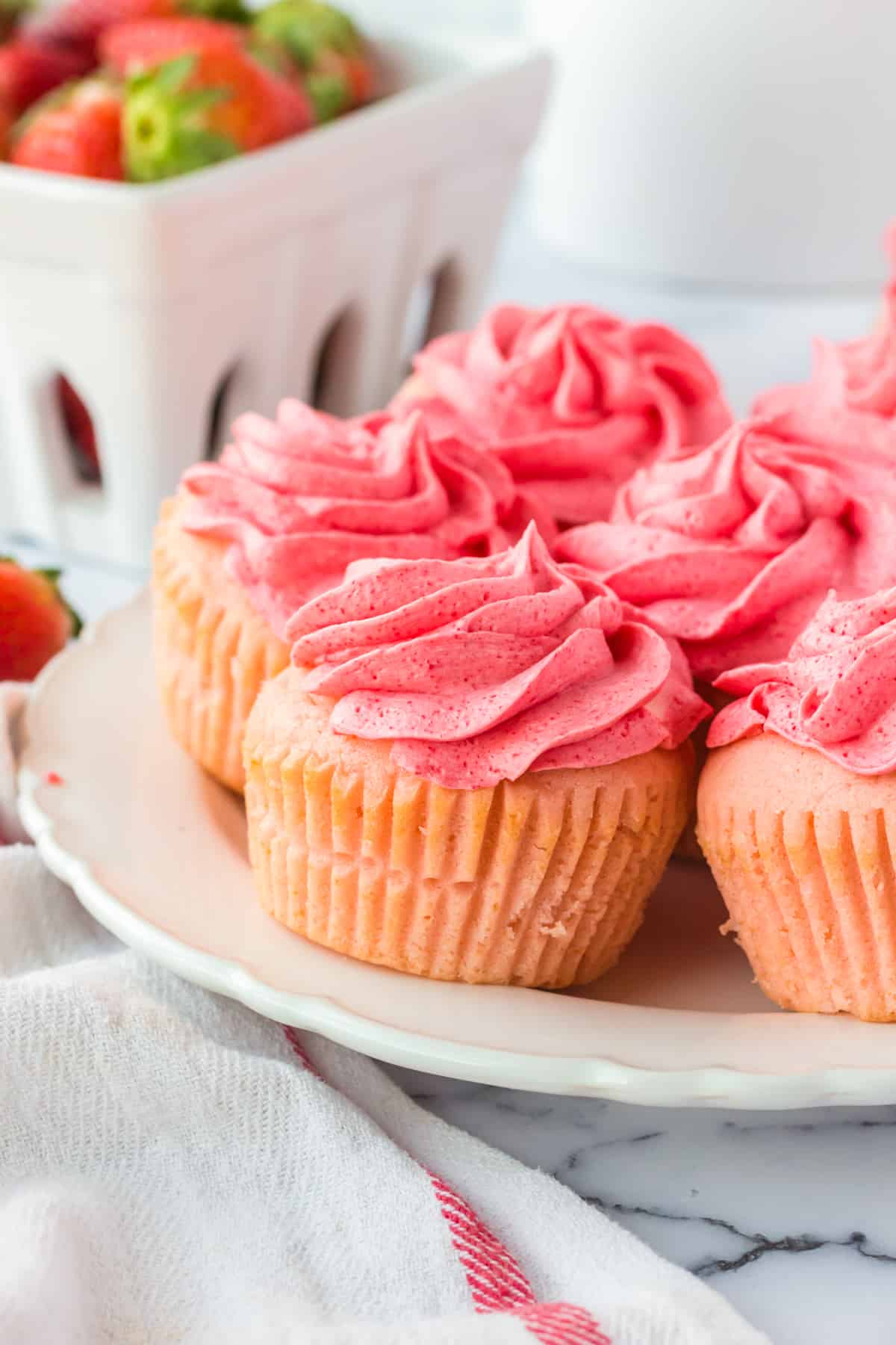 Pink frosted cupcakes with fresh strawberries in the background