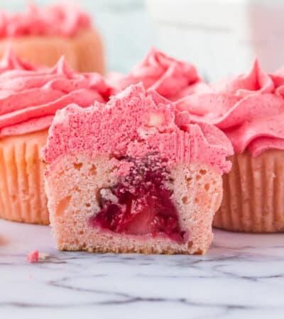 Pink cupcake with pink frosting sliced in half to show whole strawberry in the center.