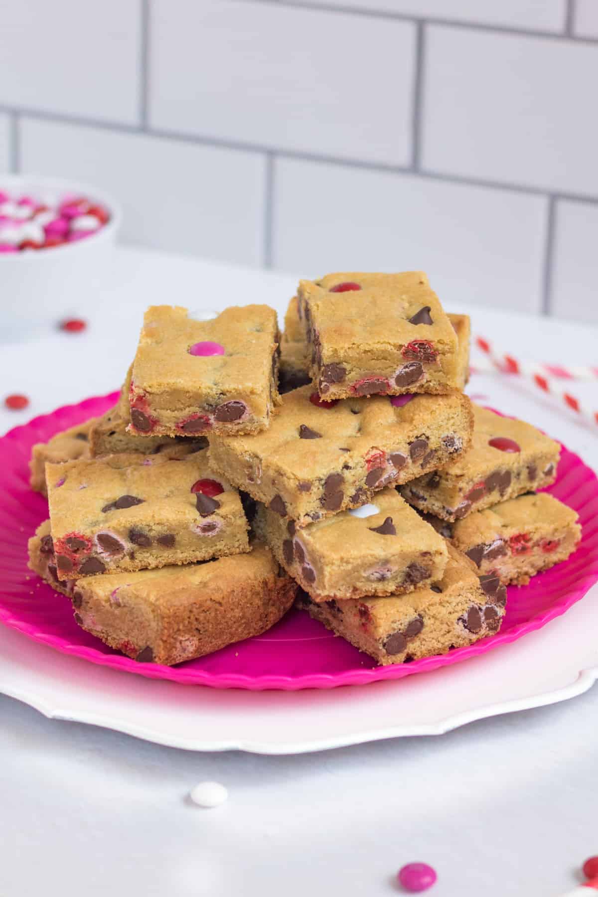 Valentines Day Cookie Bars arranged on a pink serving platter with red and pink paper straws and M&M candies around them.