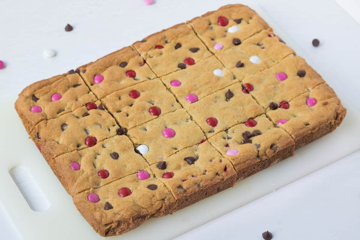 chocolate chip cookie bars with Valentine's M&M candies on a cutting board, sliced into 12 bars.