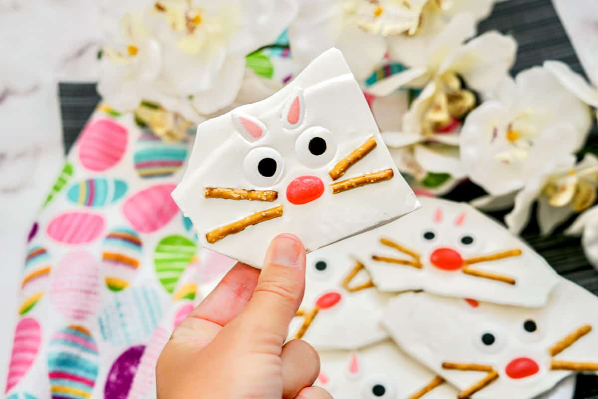 Hand holding piece of easter bark with bunny face made from pretzel sticks, jelly beans, candy ears, and candy eyes.