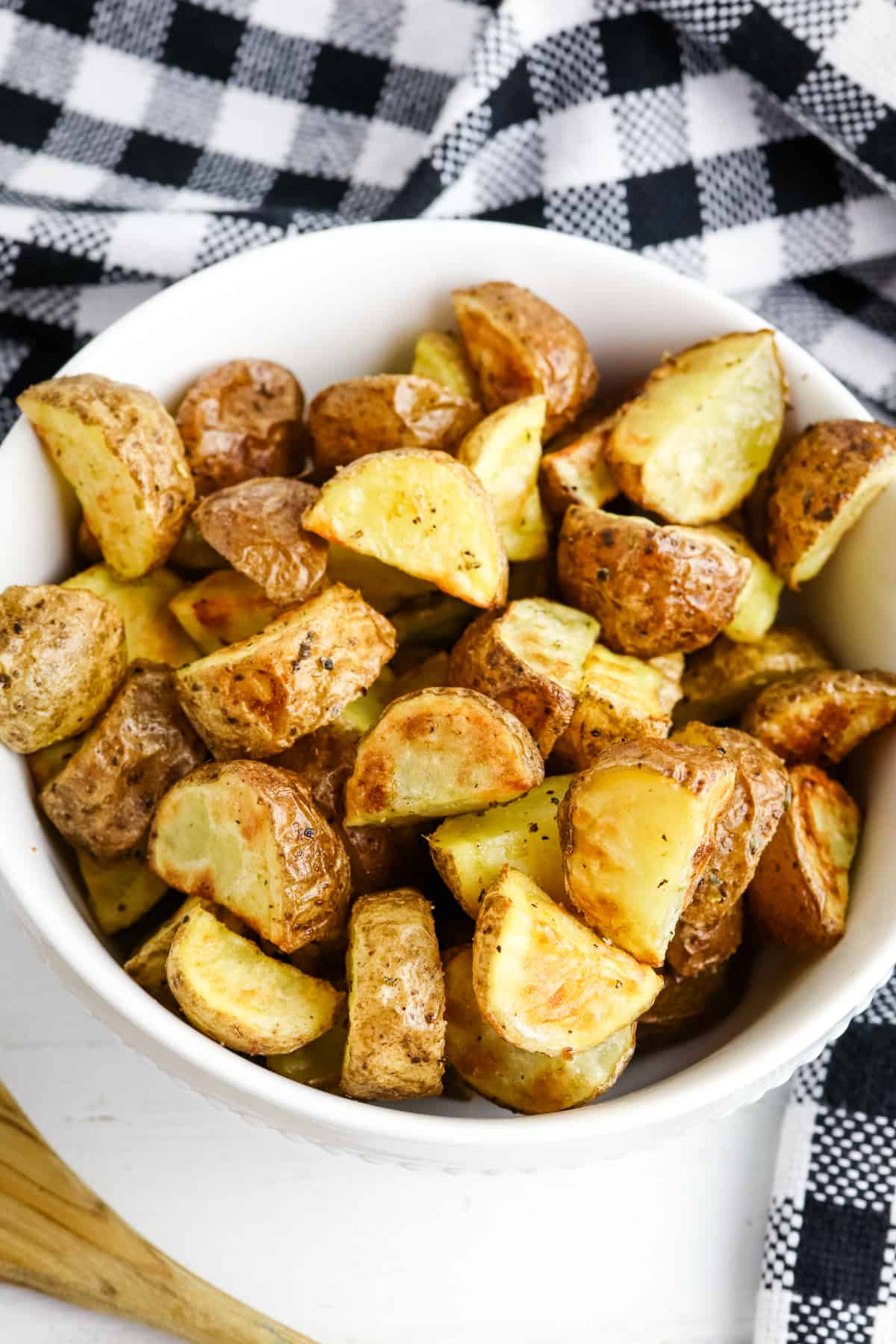 Crispy Air Fryer roasted potatoes in white bowl with black and white linen on the side.