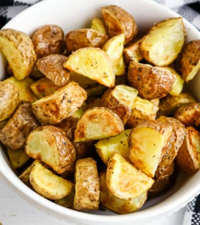 Air fryer roasted potatoes with Italian seasoning in white servings bowl.