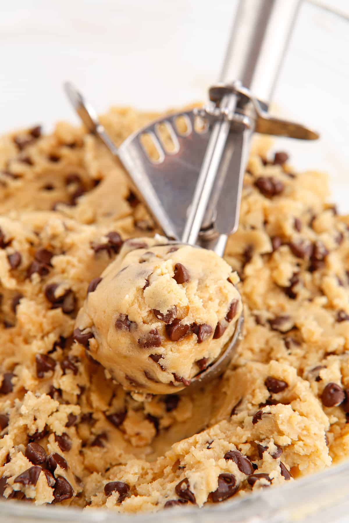 Cookie scoop scooping up cookie dough with mini chocolate chips.