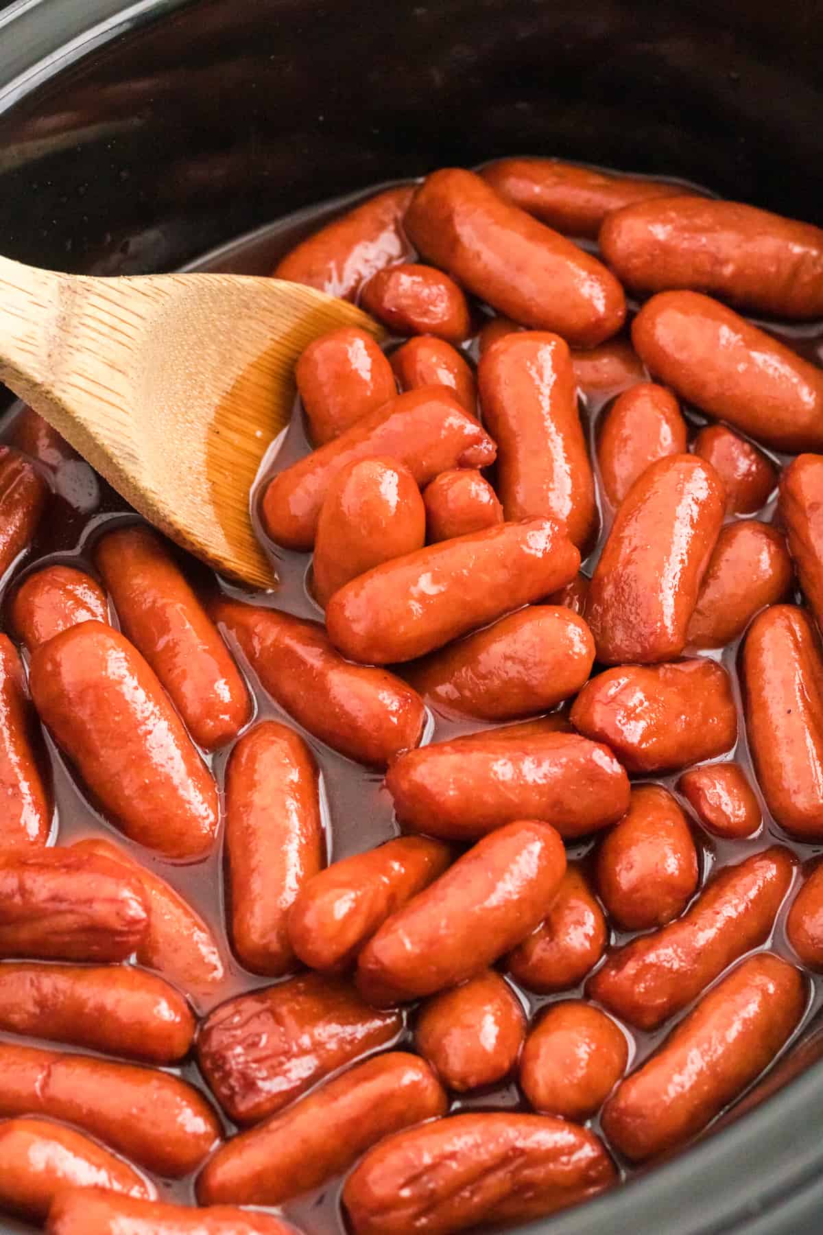 Little Smokies Cocktail Sausages in a slow cooker with a wooden spoon.