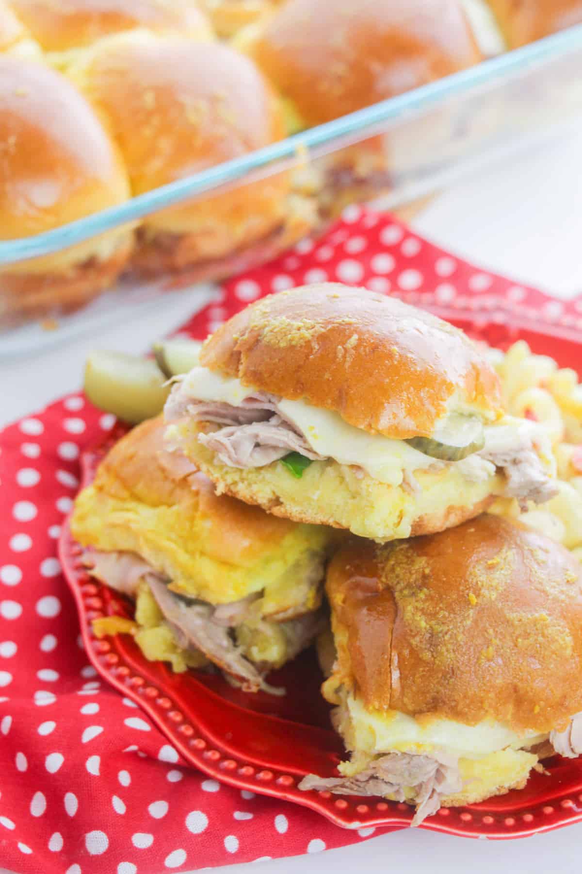 Hawaiian roll cuban sliders stacked on top of one another served on a red plate with a pickle.