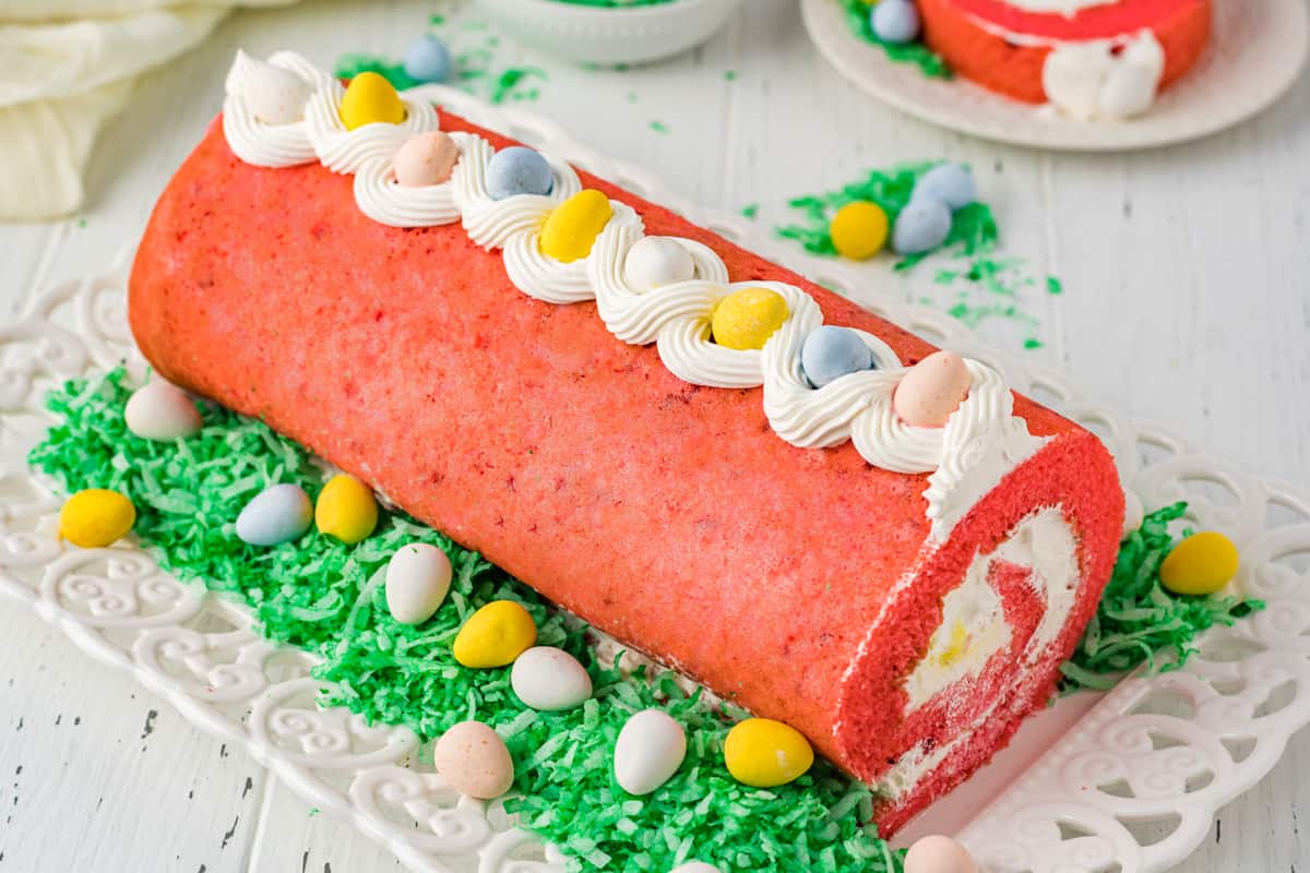 Easter cake roll with candy eggs and green shredded coconut around it on the platter to look like grass.