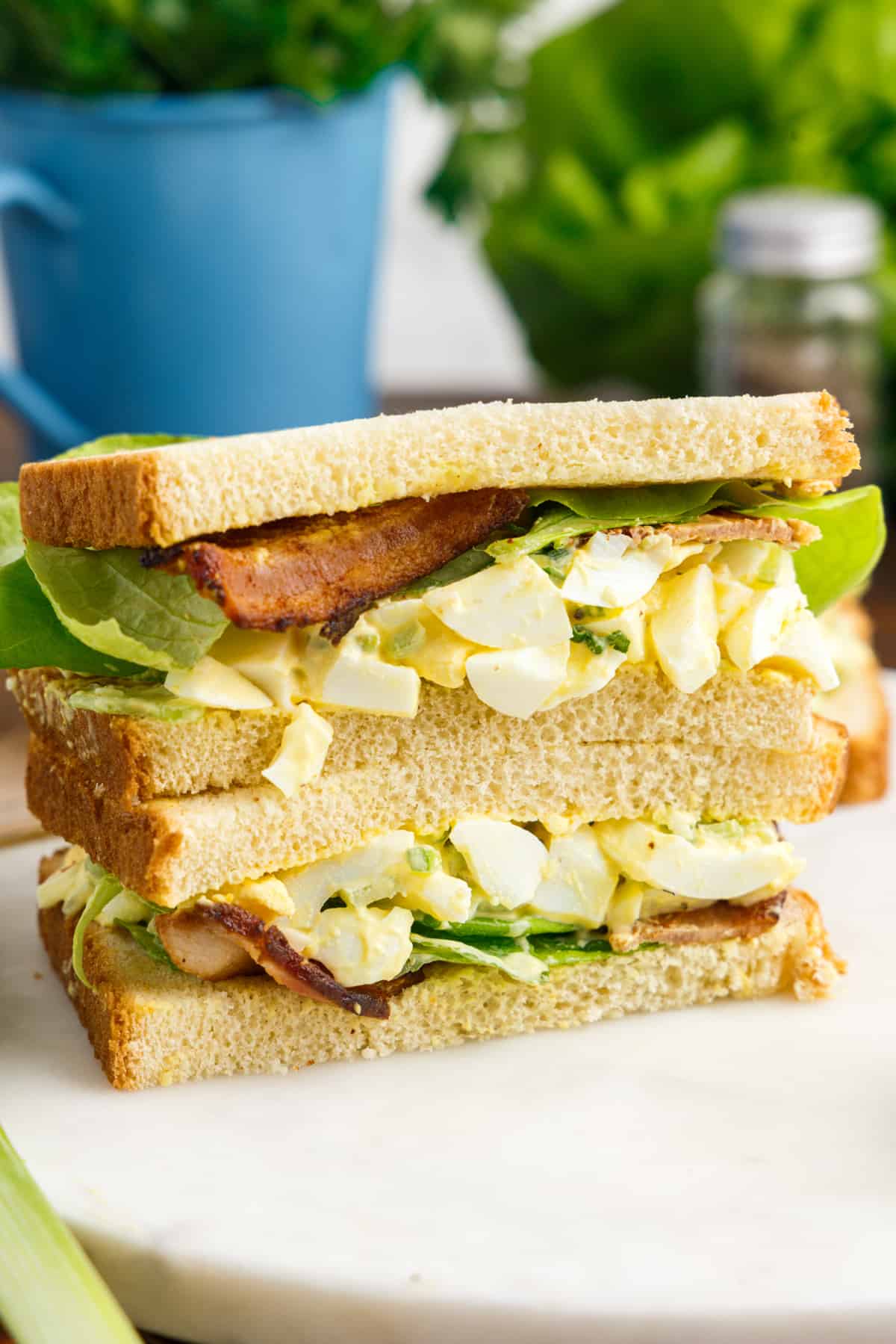 Two halves of egg salad sandwich stacked on top of one another on white plate.