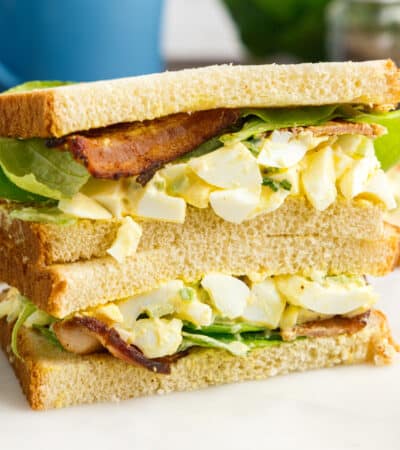 Two egg salad sandwich with bacon and lettuce stacked on top of one another.
