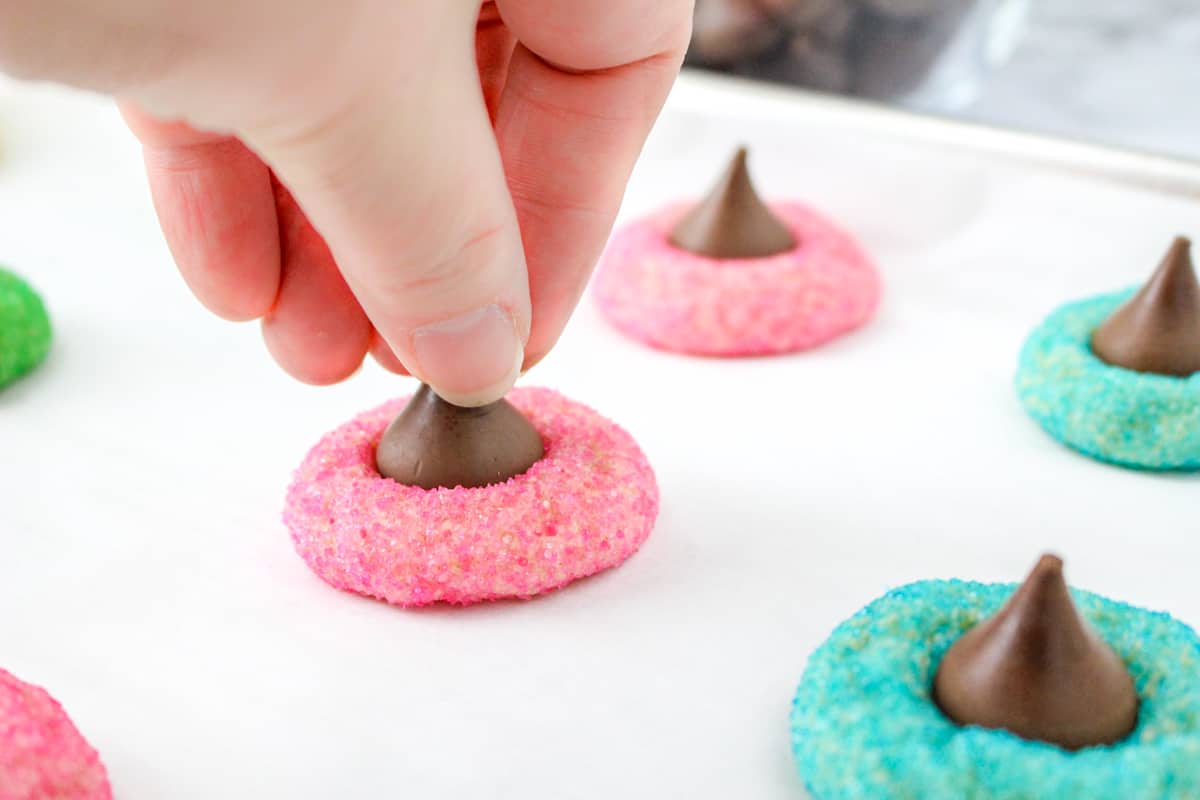 Hand pressing Hershey Kiss into the top of pink cookie.