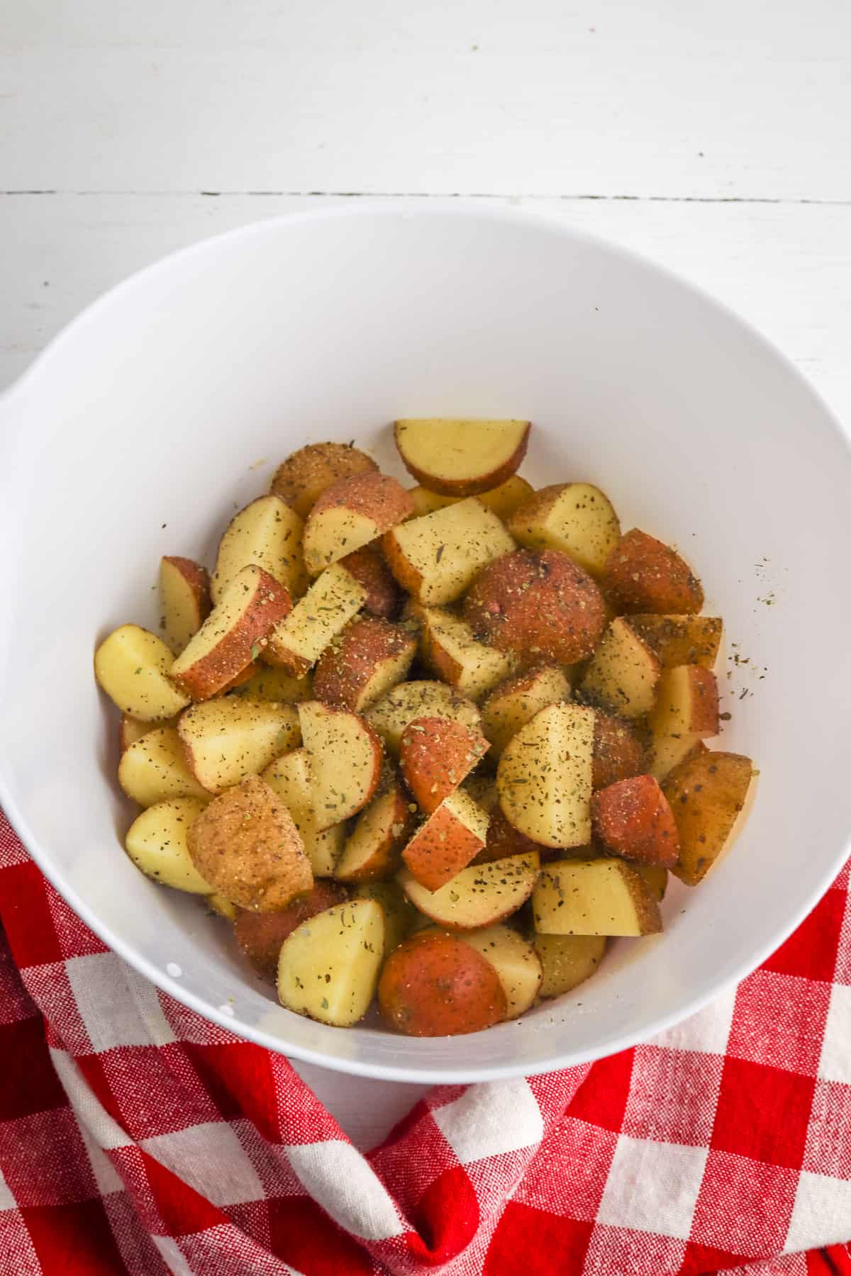 Chopped potatoes coated with oil and seasoning in a white mixing bowl.