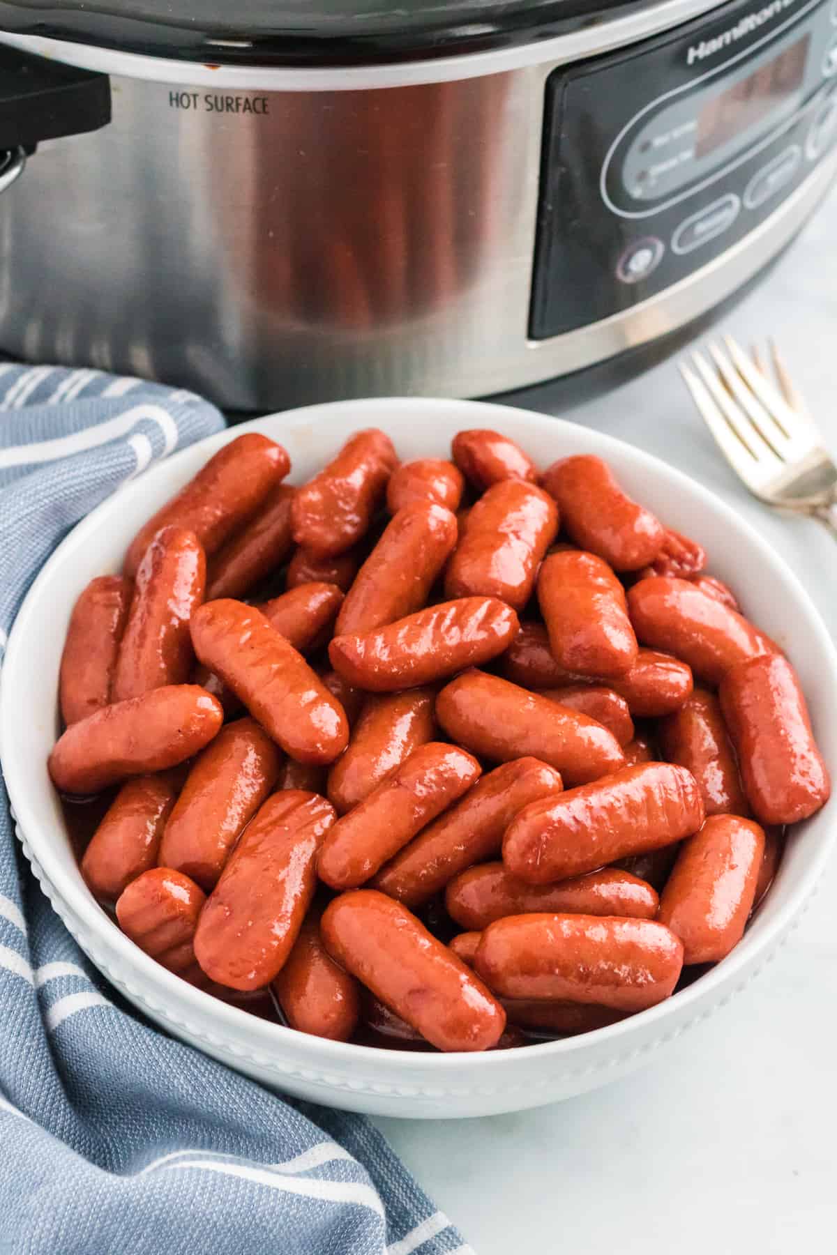 Crockpot little smokies with barbecue sauce and grape jelly in a white bowl with slow cooker in the background.