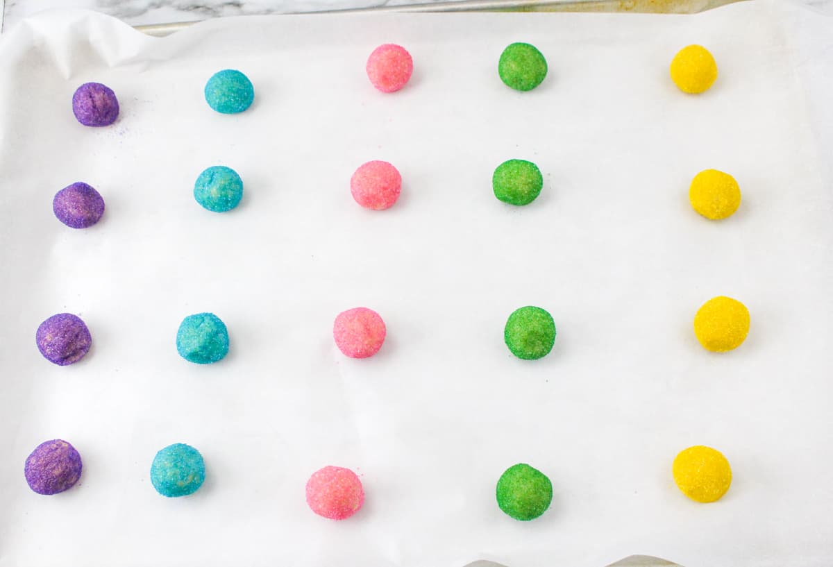 Purple, blue pink, green. and yellow sugar covered dough balls on parchment lined baking sheet.