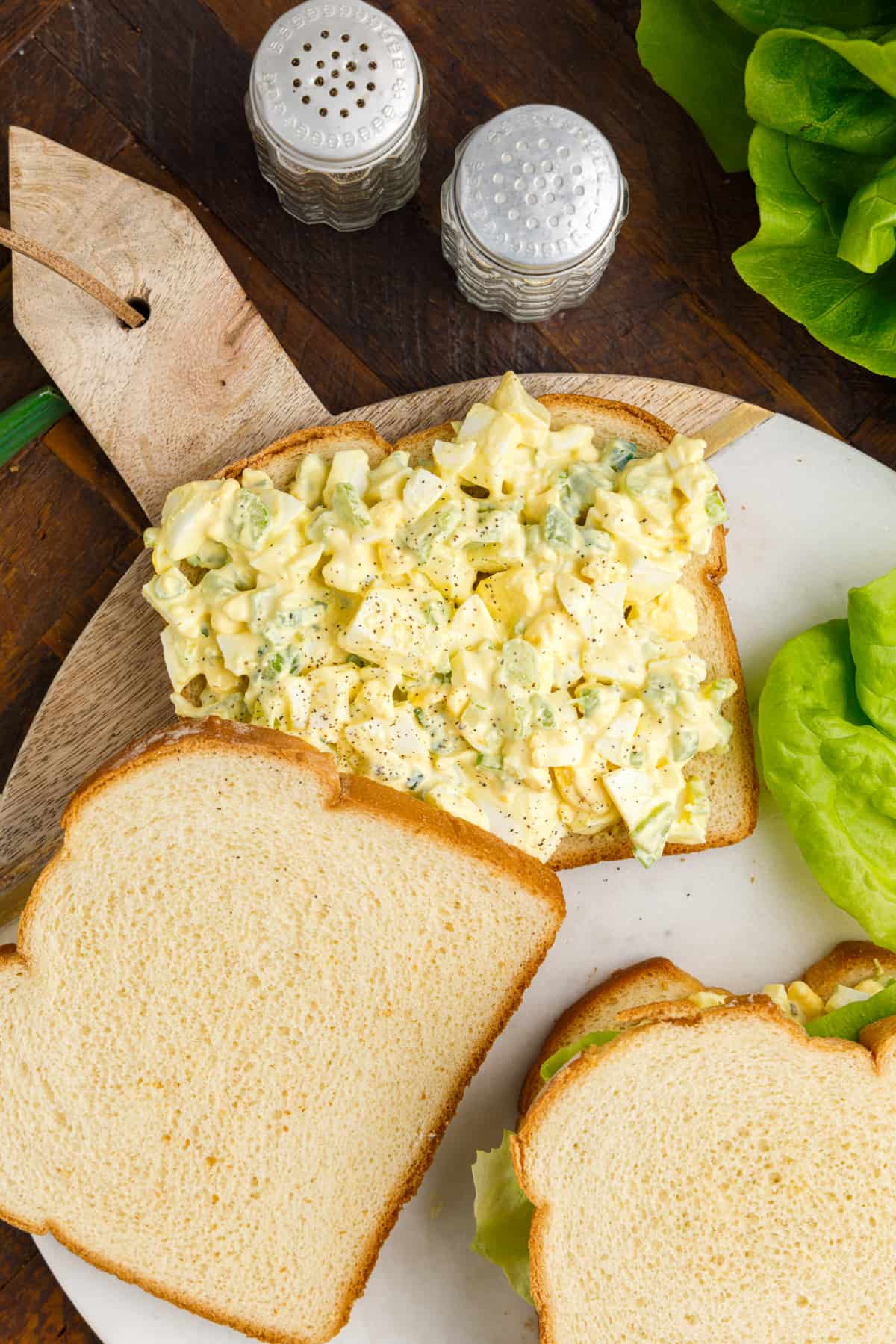 Egg salad with salt and pepper on sandwich bread with lettuce and additional slices of bread around it.