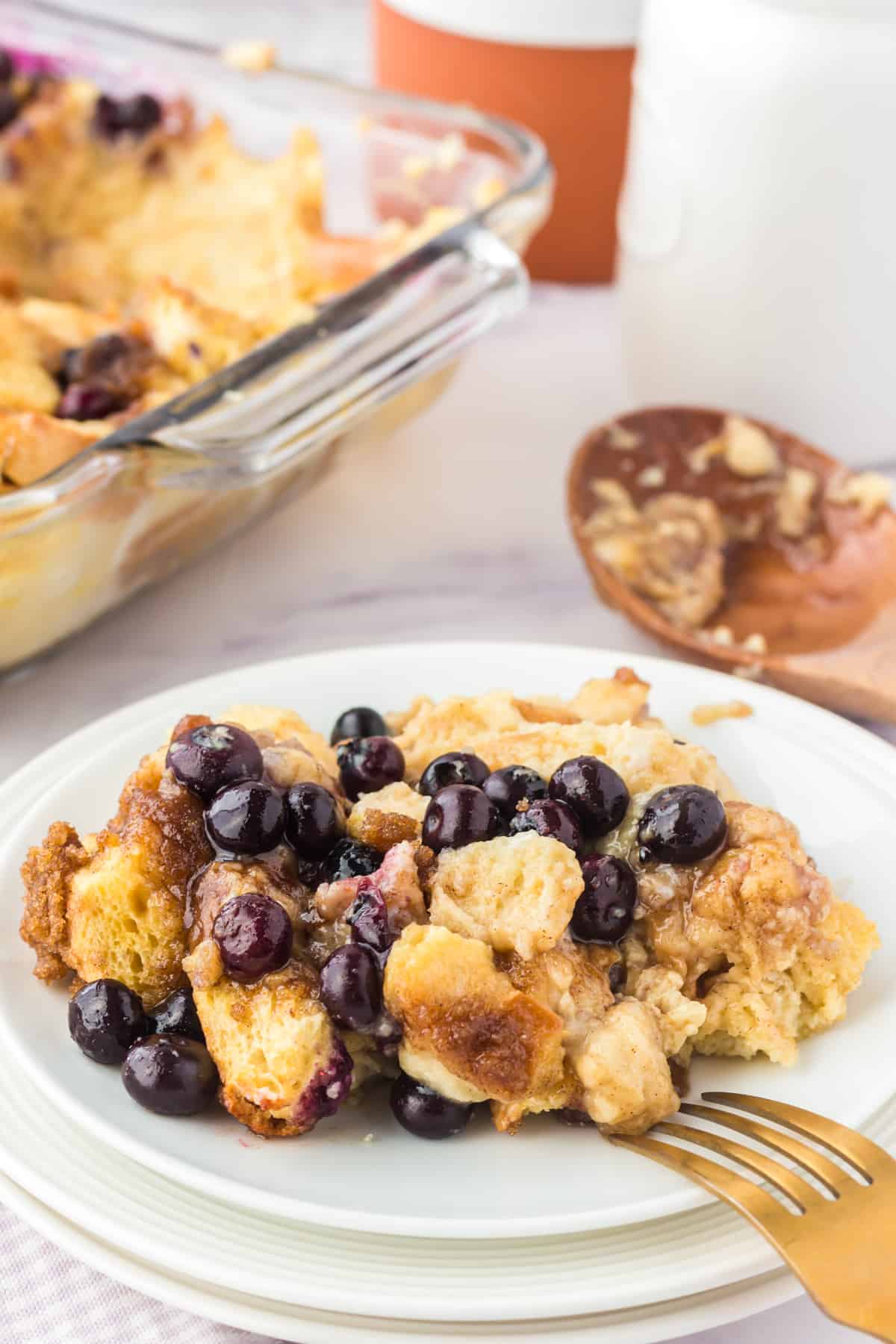 Blueberry overnight french toast casserole on white plate with baking dish in background.