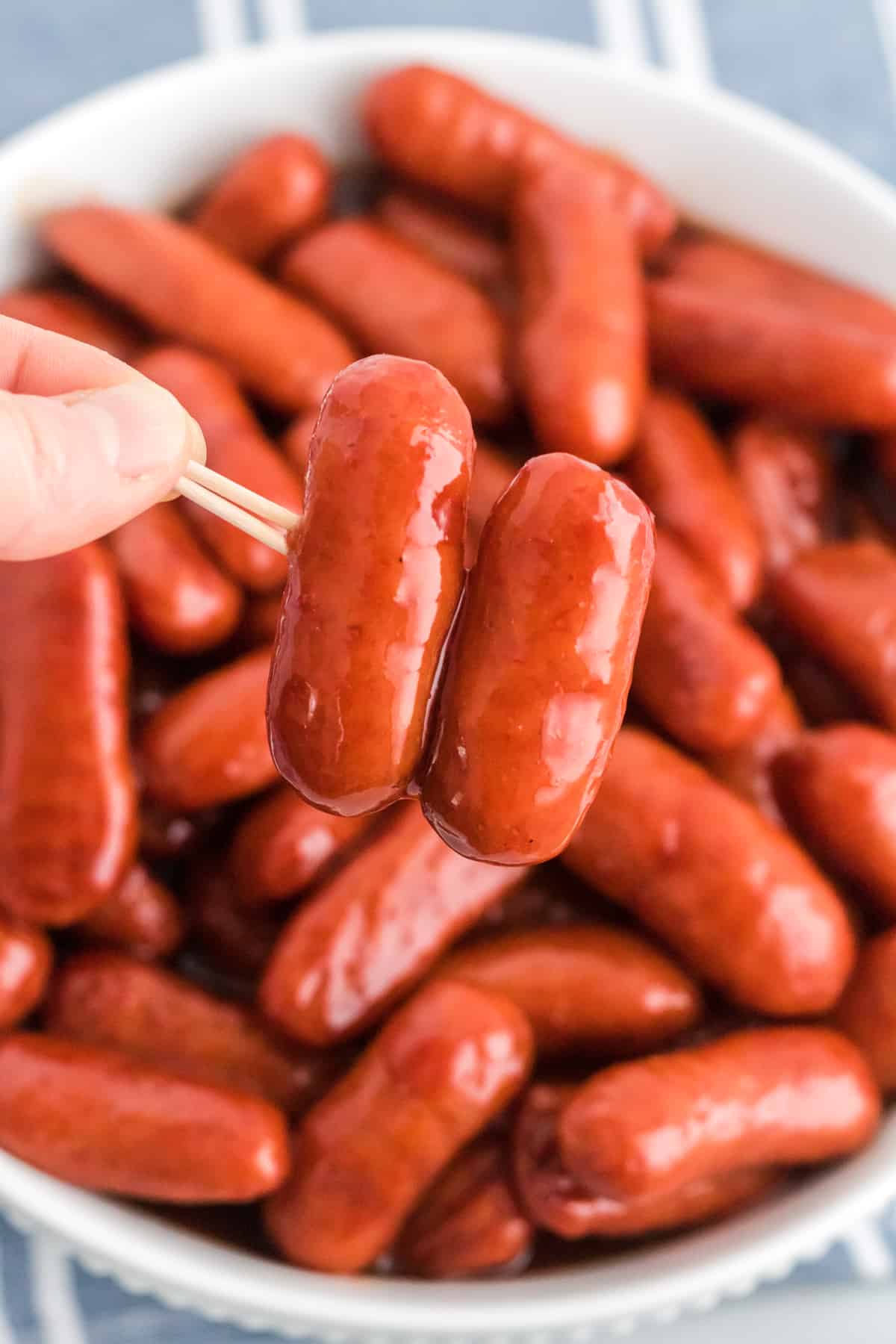 Two cocktail weenies on a toothpick with rest of slow cooker lil smokies in a bowl in the background.