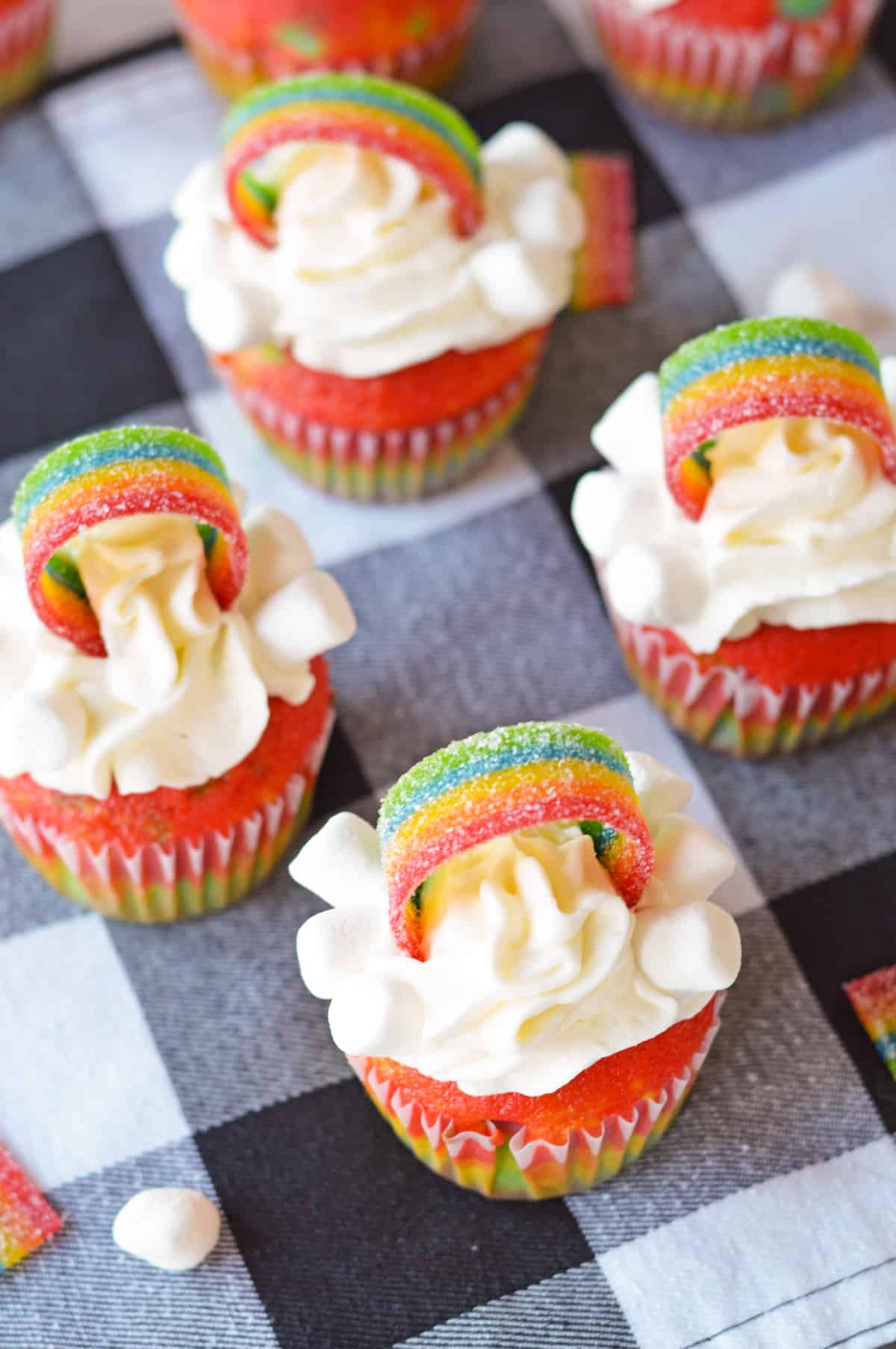 Four cupcakes decorated with rainbows, miniature marshmallows, and white frosting on top.