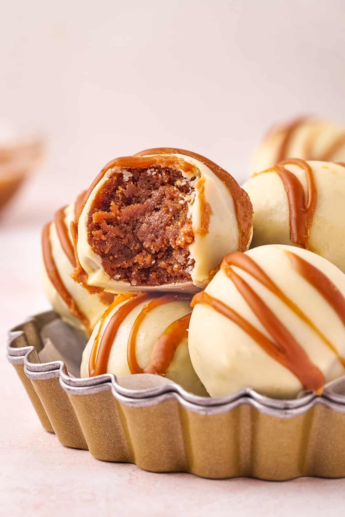 Biscoff Truffles made with crushed Biscoff cookies, cookie butter, and cream cheese with a white chocolate coating. One of the truffles has a bite taken out of it.